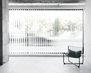 Modern office space with vertical blinds providing light control and privacy, showcasing a minimalist chair in a bright, open environment.