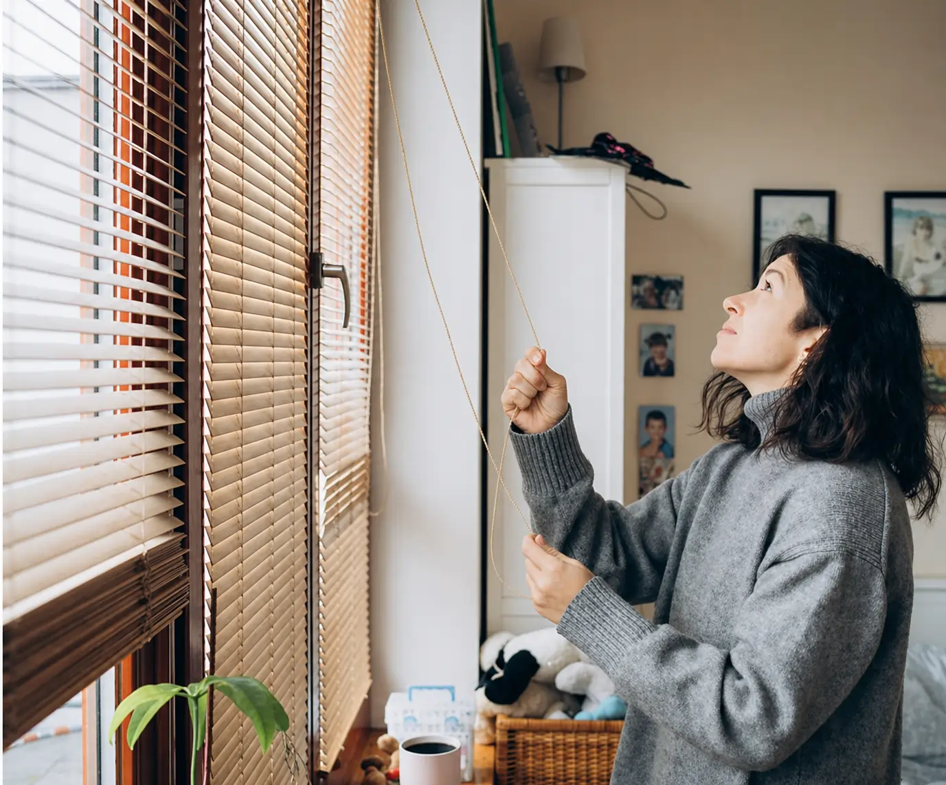 Person adjusting window blinds in a cozy home setting, showcasing Blinds as a provider of high-quality window treatments for privacy, light control, and style.