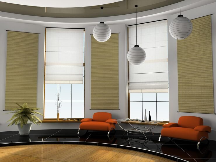 Modern living room with two orange chairs, black tiled flooring, and beige Roman blinds covering the windows. The space includes three pendant lights and a decorative plant on a table, with a minimalist design and large windows letting in natural light.